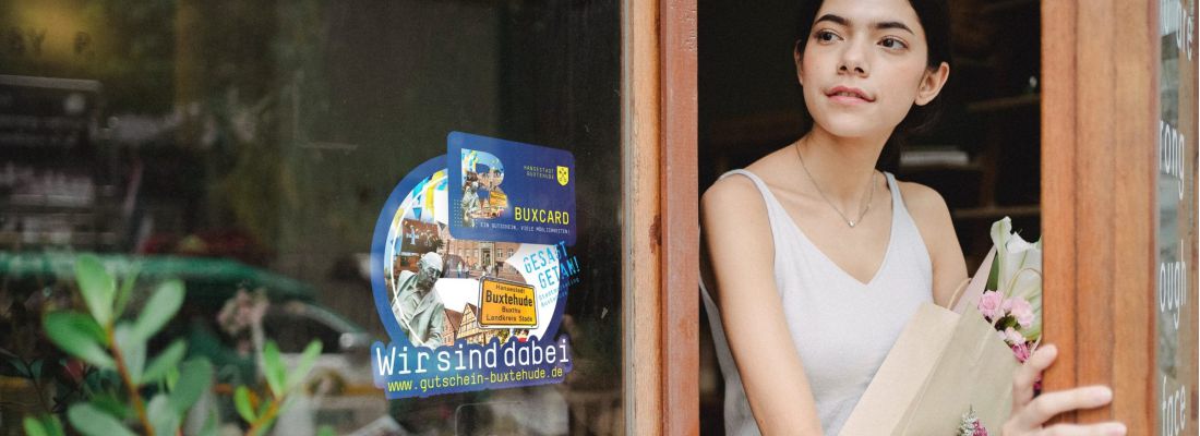 Frau mit Shopping Bag verlässt ein Geschäft, mit BUXCard Aufkleber im Schaufenster