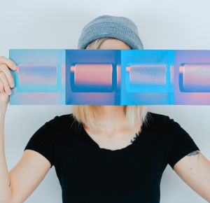 Frau hält blaues Kunstwerk vor Ihr Gesicht 