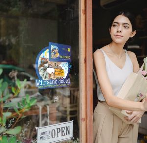 Frau mit Shoppingtasche verl&auml;sst Gesch&auml;ft mit BUXCard Aufkleber